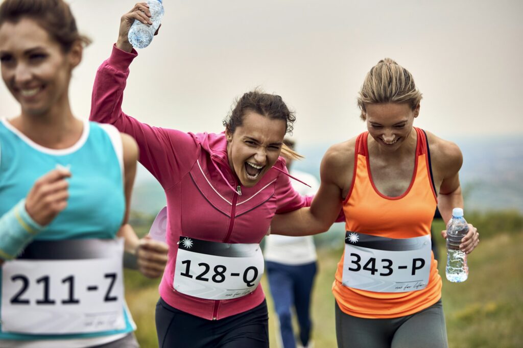 Happy athletic women having fun while running a marathon in nature.